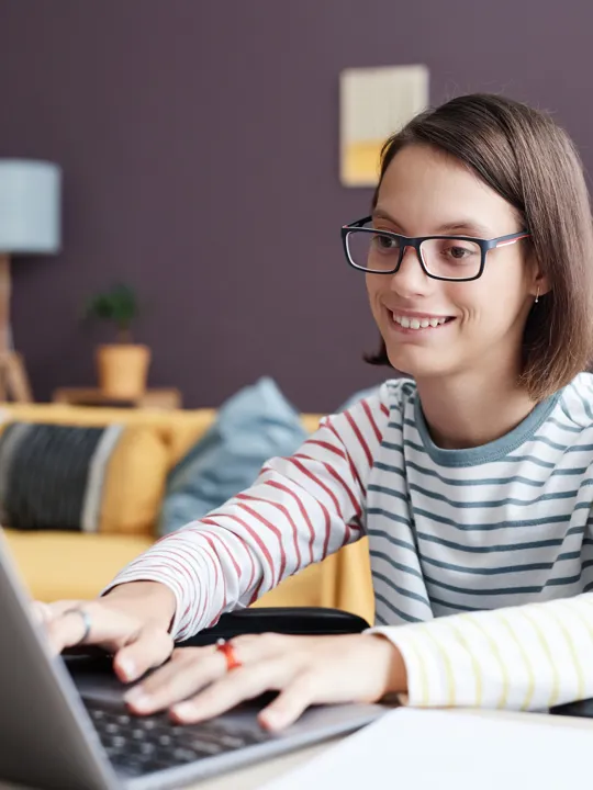 Teenage girl studying on laptop in wheelchair in comfortable home setting