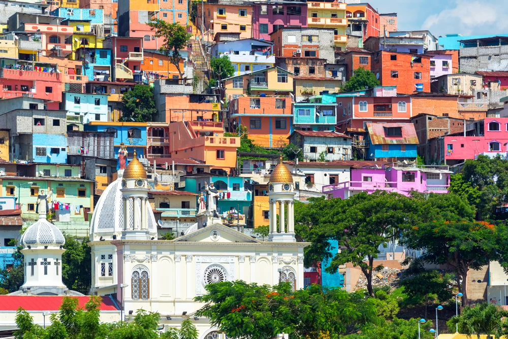A landscape view of an Ecuadorian city, with a church in the forefront, and colourful buildings in the background. 