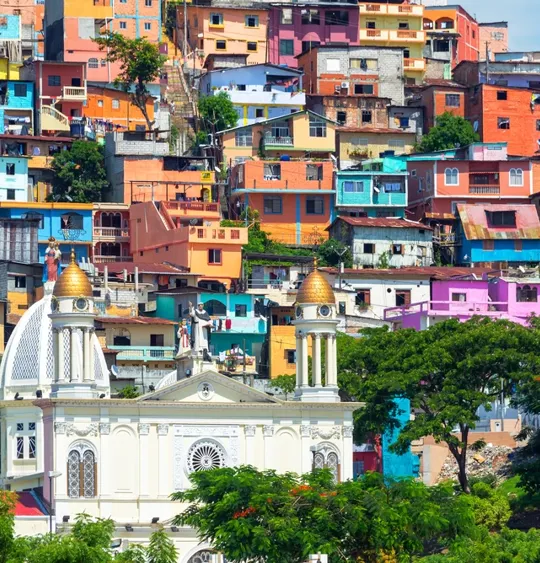 A landscape view of an Ecuadorian city, with a church in the forefront, and colourful buildings in the background.