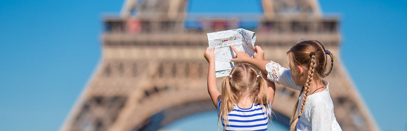 Two young girls holding a map and looking at the Eiffel Tower on a bright, sunny day.