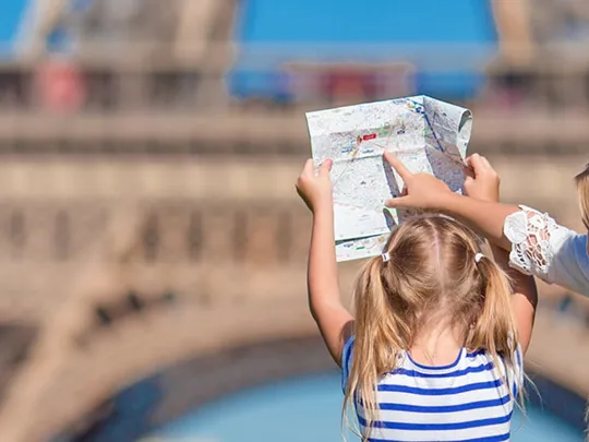 Two young girls holding a map and looking at the Eiffel Tower on a bright, sunny day.