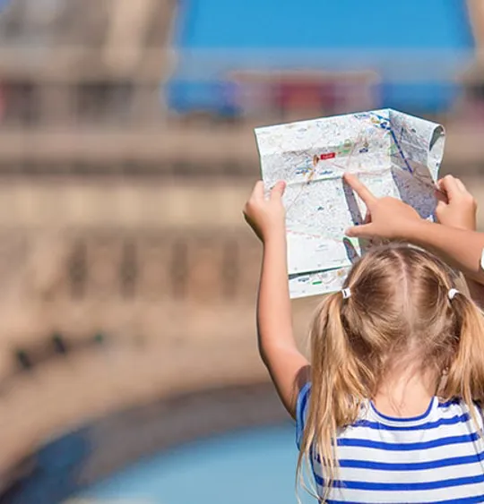 Two young girls holding a map and looking at the Eiffel Tower on a bright, sunny day.