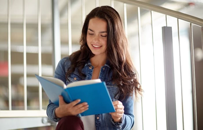 Female GCSE Level student reading from a blue book.