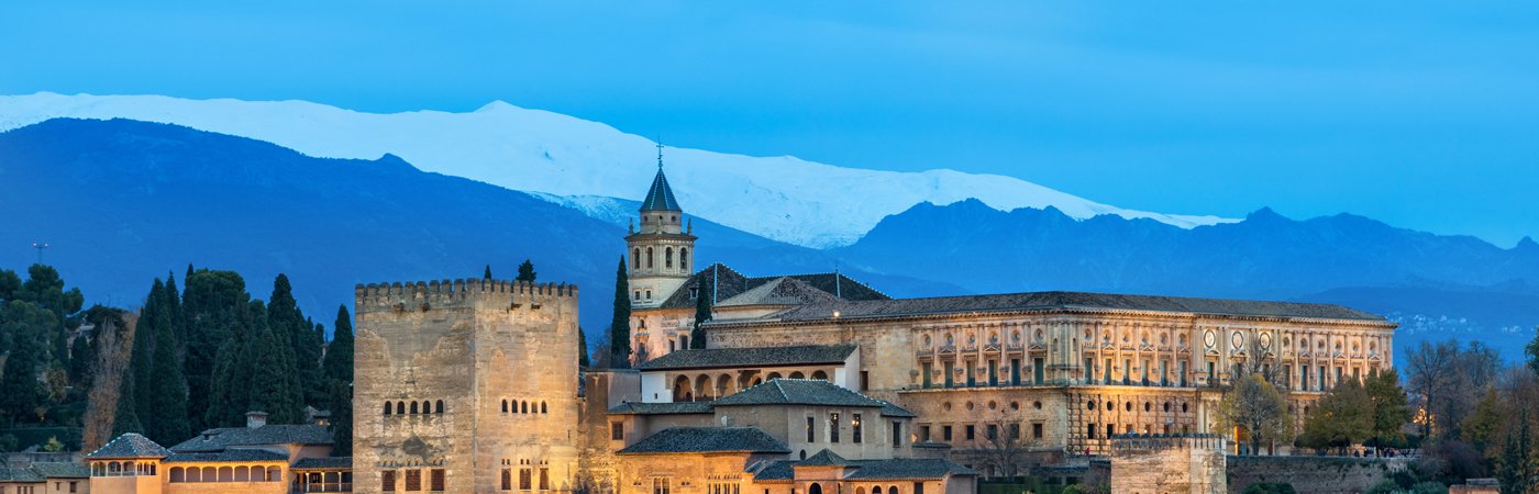 Scenic view of the Alhambra Palace with snow-capped mountains in the background at dusk.