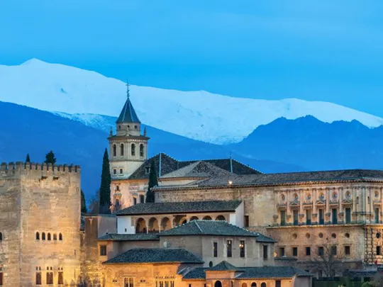 Scenic view of the Alhambra Palace with snow-capped mountains in the background at dusk.