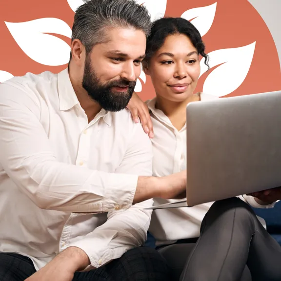 Couple seated closely on a sofa, attentively viewing a laptop screen in a relaxed home setting.