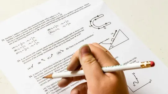 A picture of someone's hand holding a pencil above an exam paper.