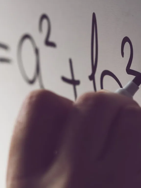 Close-up shot of a hand writing a mathematical equation, c 2 =a 2 +b 2 , on a white board with a black marker. The equation is a representation of the Pythagorean theorem.
