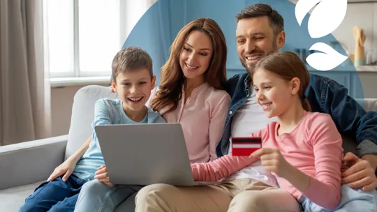 A happy family sitting together on the sofa, enrolling their children in an online school with a laptop.