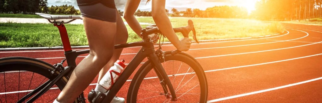 A close up image of a track cyclist riding on a track as the sun is starting to set. 