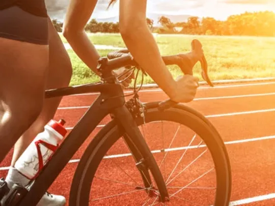 A close up image of a track cyclist riding on a track as the sun is starting to set.