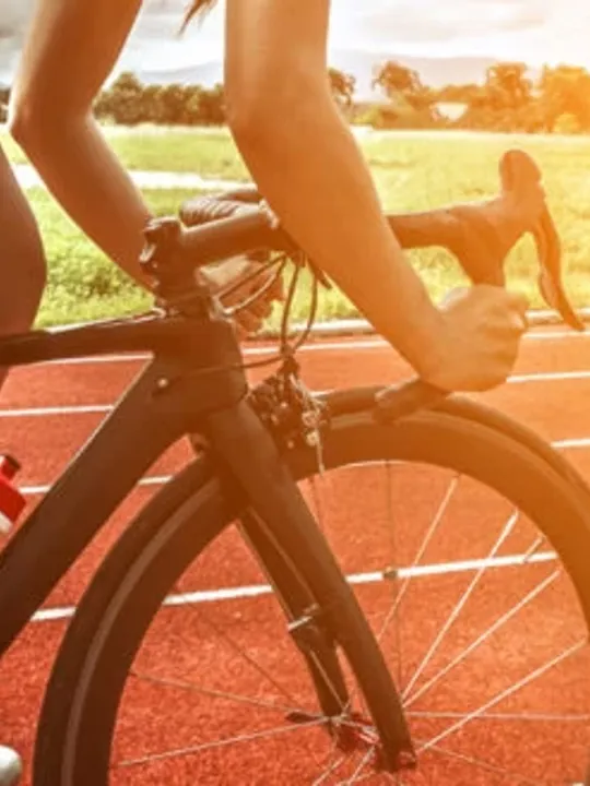 A close up image of a track cyclist riding on a track as the sun is starting to set.