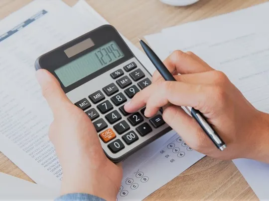 Person calculating figures on a printed statement using a large calculator.