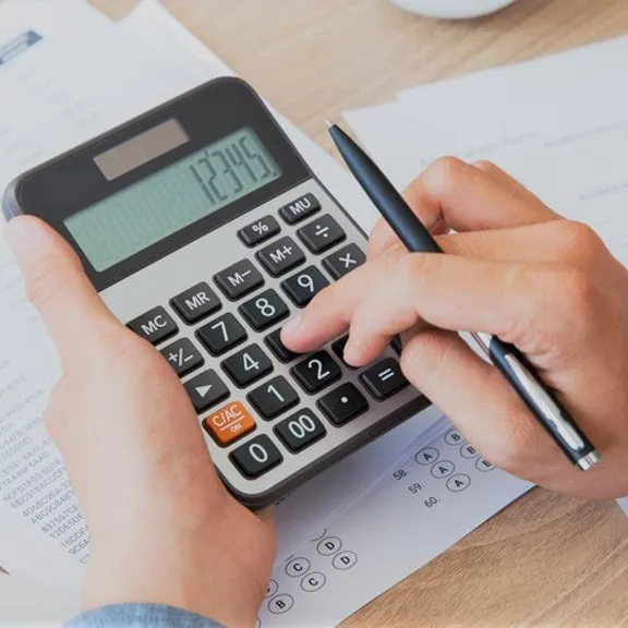 Person calculating figures on a printed statement using a large calculator.