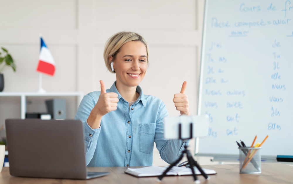 Female online French tutor smiling and giving thumbs-up during an online tutoring session.