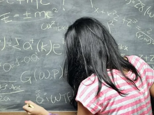 A maths student writing her equations on a blackboard.