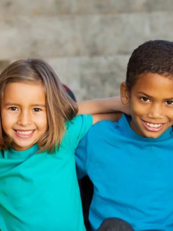 Four children sitting outdoors with arms around each other, smiling and enjoying friendship
