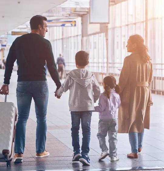 Family of four walking hand in hand through airport with travel bags
