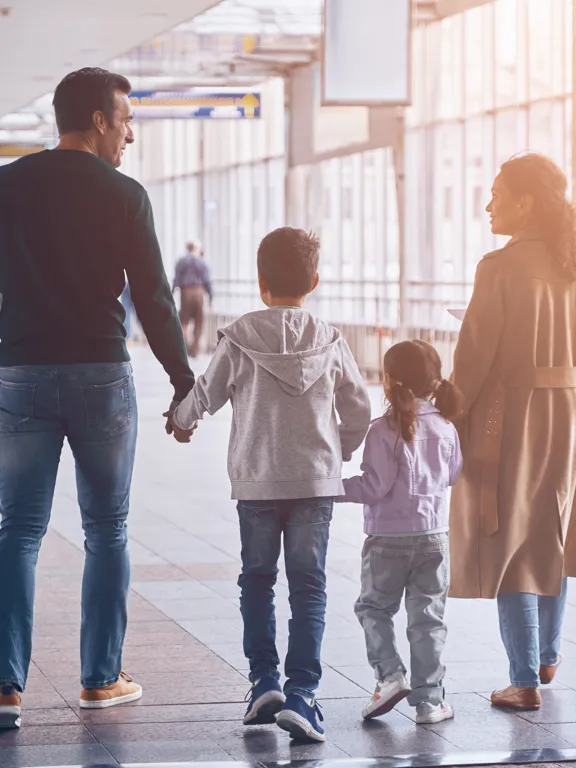 Family of four walking hand in hand through airport with travel bags
