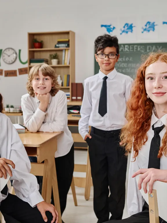 Diverse group of students in school uniforms smiling in a cozy classroom, representing the close-knit community of small independent or local schools with Pamoja.