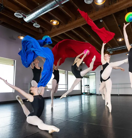 Ballet dancers mid-performance in studio with flowing red and blue fabric
