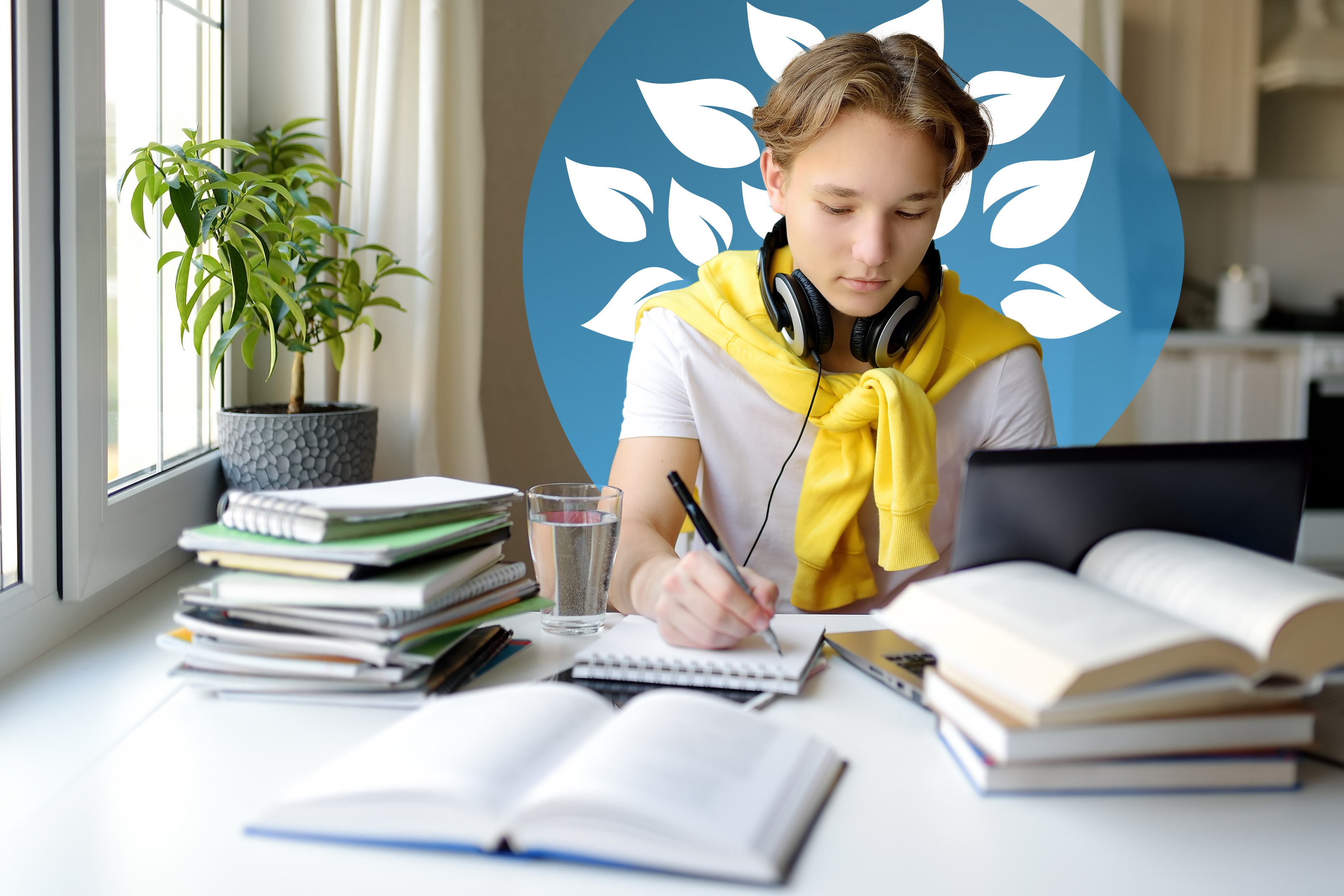 A teenage student with headphones sits at a desk at home, writing in a notebook while studying online with a laptop and books.