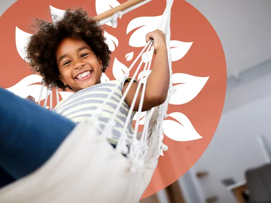 Happy child relaxing in a hammock at home, smiling confidently at the camera.