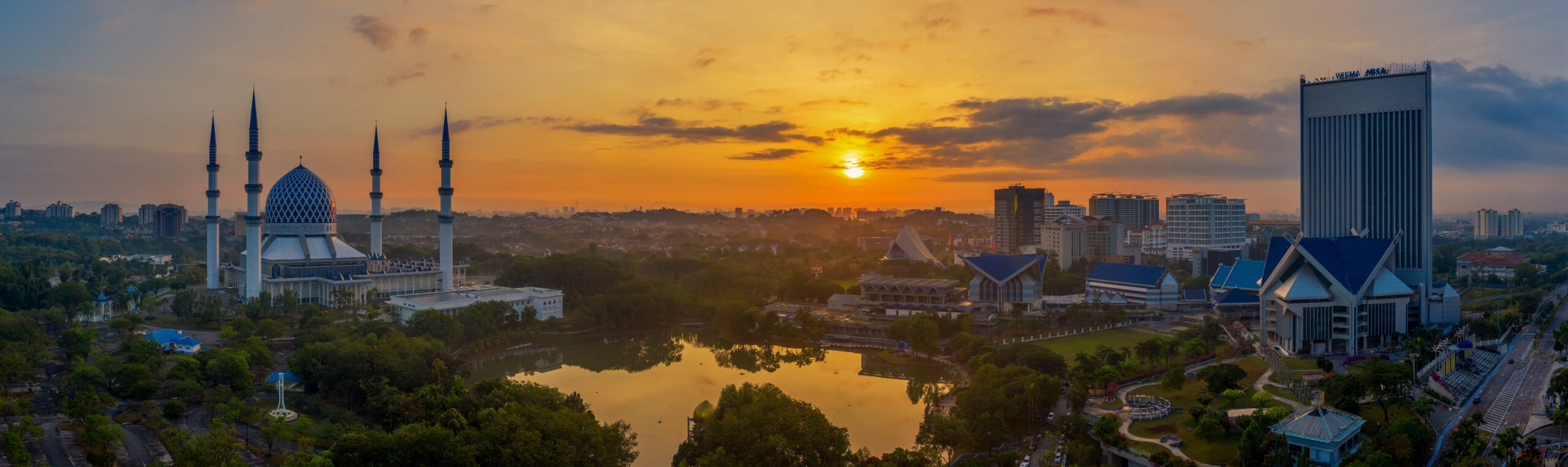 Panoramic sunrise view of Shah Alam, Selangor, featuring the prominent Sultan Salahuddin Abdul Aziz Mosque, a lake, and the city skyline, illustrating the environment for homeschooling families in the region