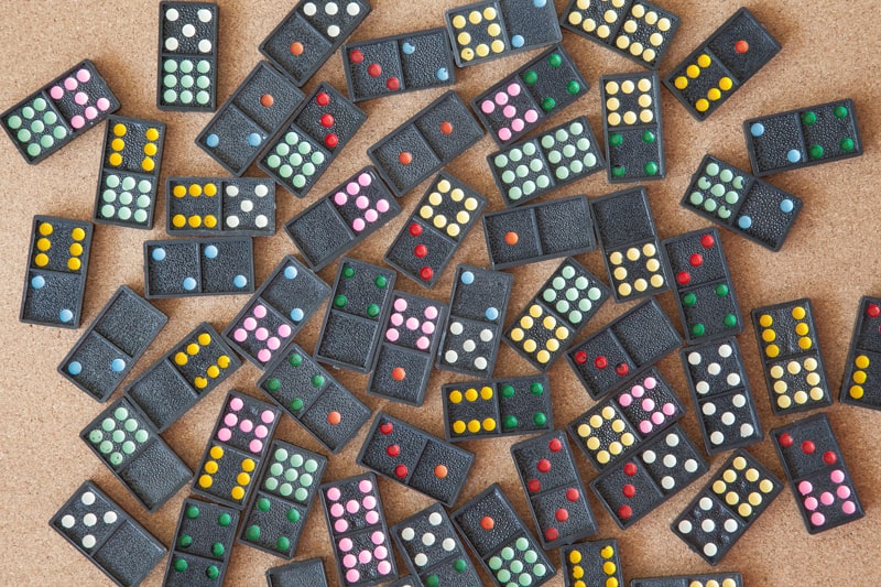 Scattered collection of colourful dot dominoes laid out on a corkboard surface