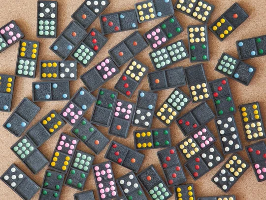 Scattered collection of colourful dot dominoes laid out on a corkboard surface