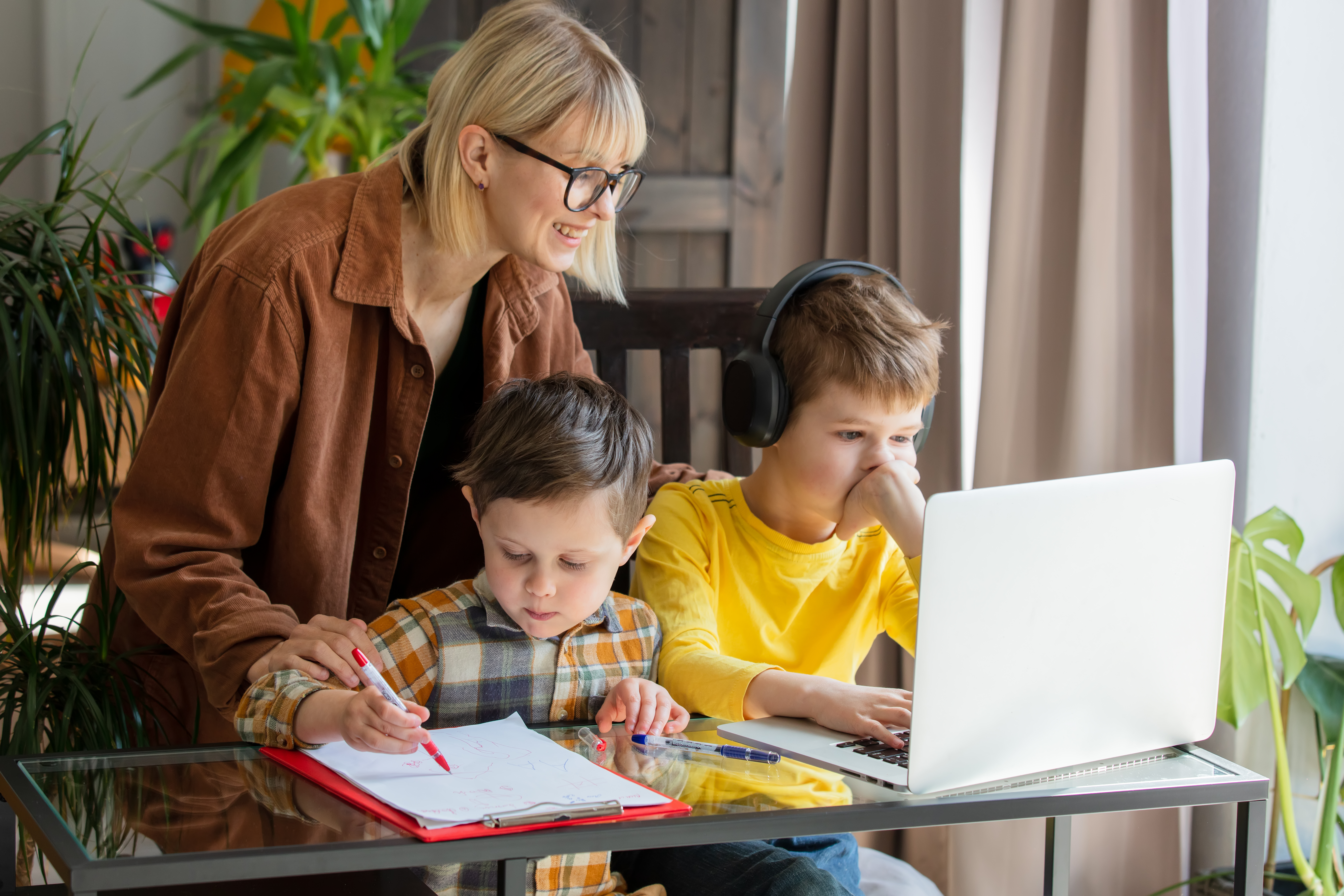Mother guiding sons during home learning with laptop and written work