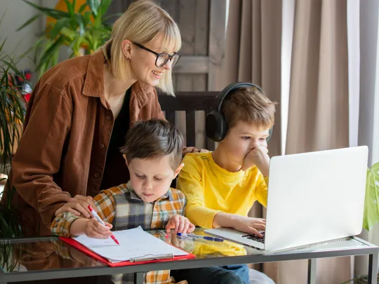 Mother guiding sons during home learning with laptop and written work