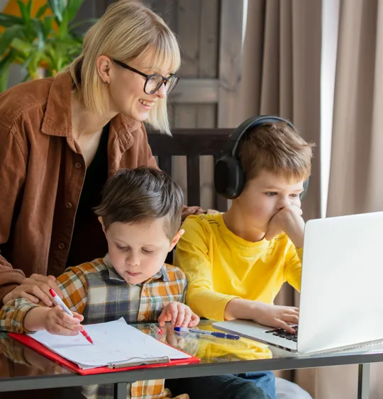 Mother guiding sons during home learning with laptop and written work