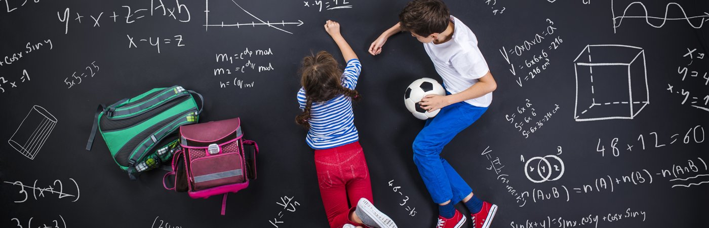 Two children lying on the floor beside rucksacks, surrounded by maths formulas drawn on a chalkboard