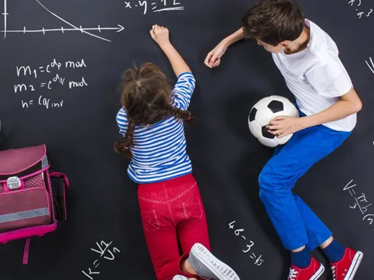 Two children lying on the floor beside rucksacks, surrounded by maths formulas drawn on a chalkboard