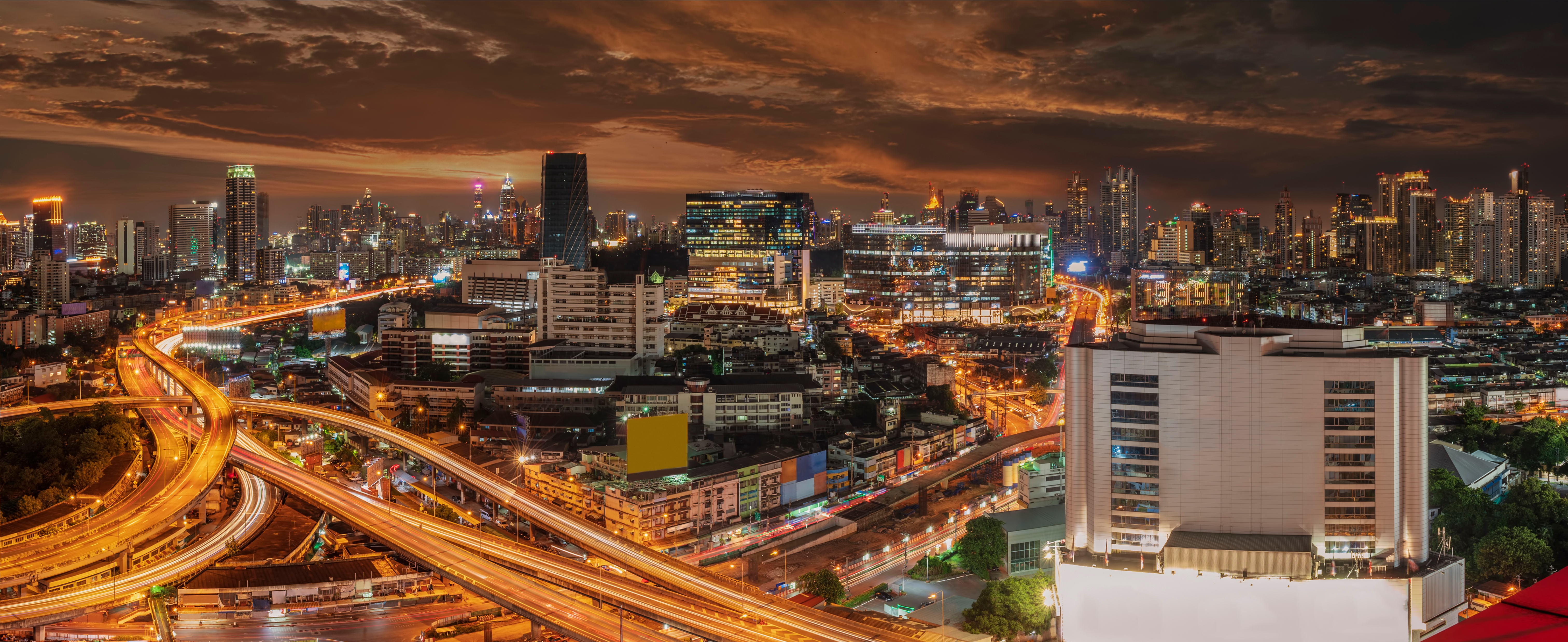 Illuminated Bangkok cityscape at night with glowing highways and high-rise buildings.
