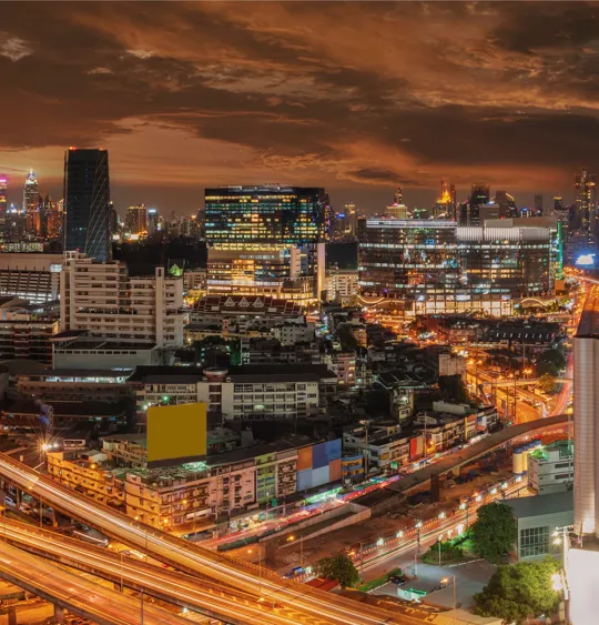 Illuminated Bangkok cityscape at night with glowing highways and high-rise buildings.
