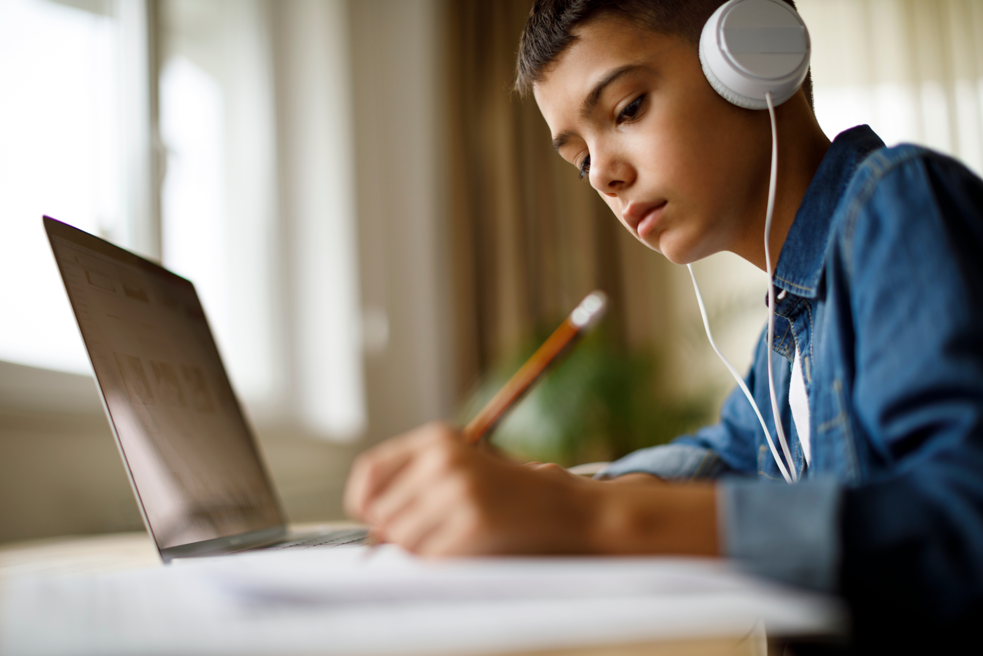 A photograph of a young boy wearing headphones studying at his bedroom desk.