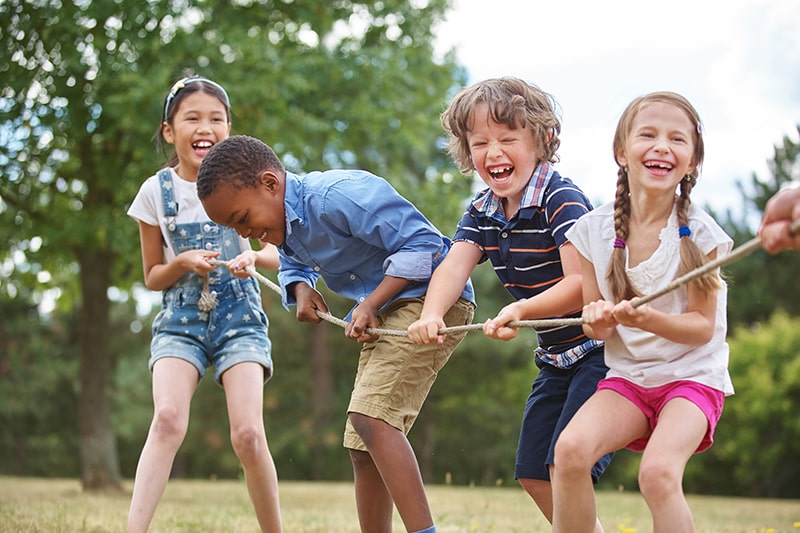 Group of children playing tug of war outdoors, laughing and enjoying teamwork in a sunny park
