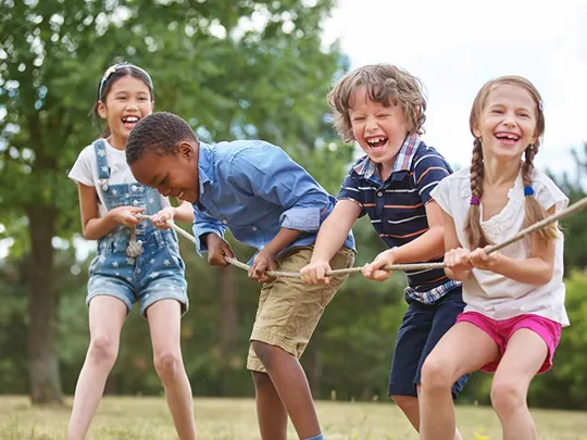Group of children playing tug of war outdoors, laughing and enjoying teamwork in a sunny park