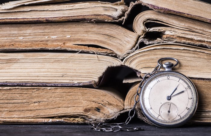 Old and damaged books stacked on top of each other, with a stop watch in front of them, showing the passing of time. 