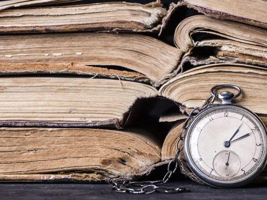 Old and damaged books stacked on top of each other, with a stop watch in front of them, showing the passing of time.