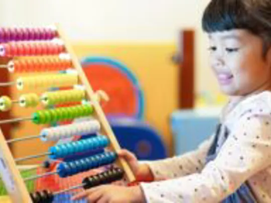 A photograph of a Primary-age girl with black hair playing with a large abacus.
