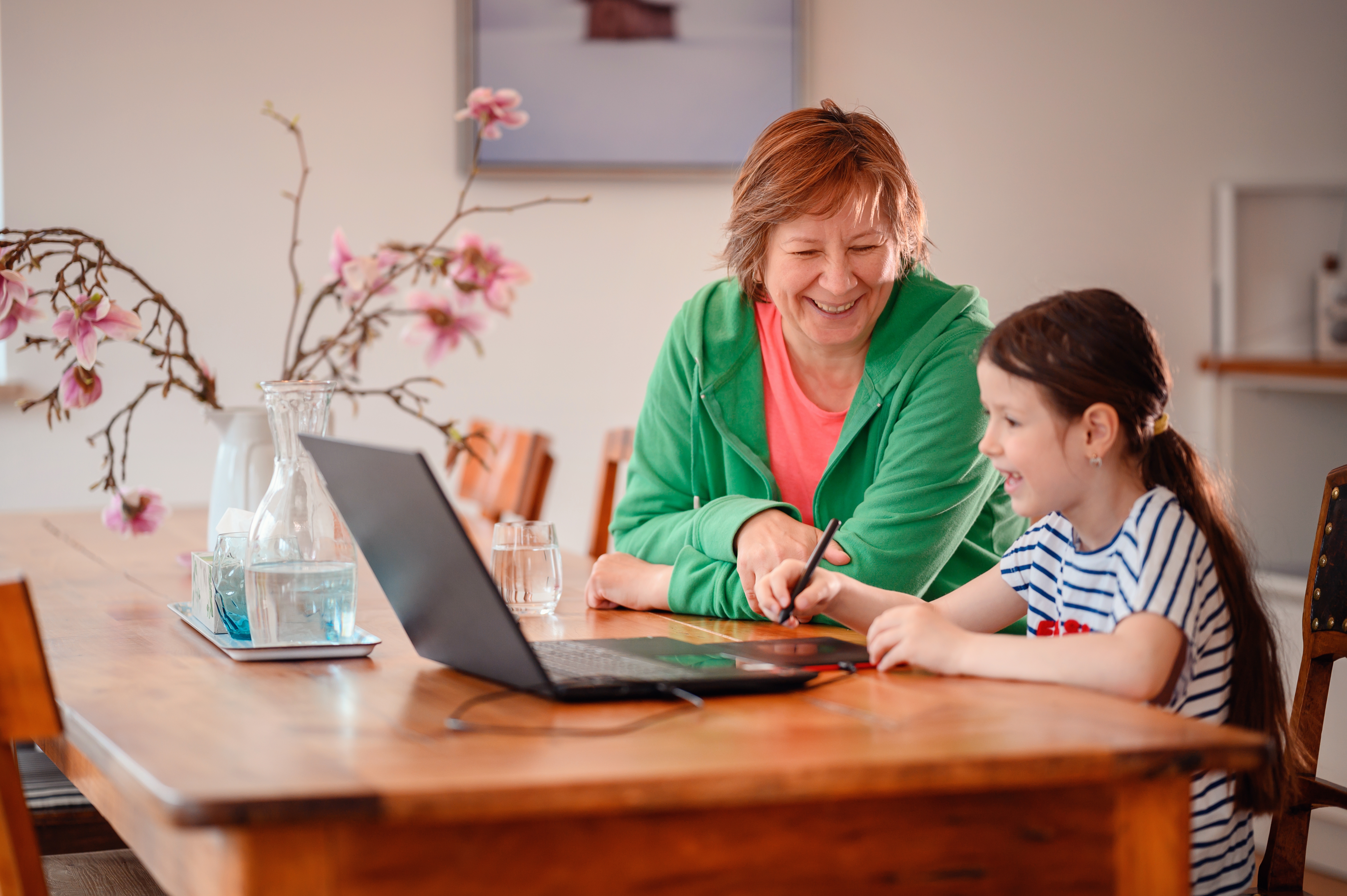 Young girl enjoying a learning activity at home with older adult and laptop