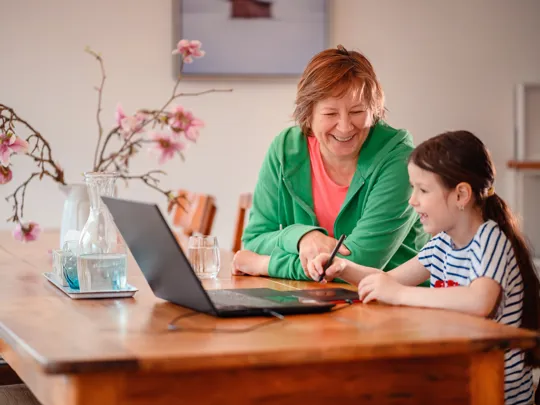 Young girl enjoying a learning activity at home with older adult and laptop