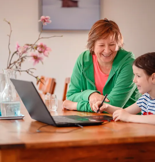 Young girl enjoying a learning activity at home with older adult and laptop