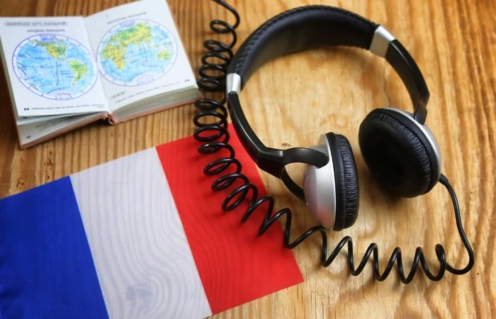 Headphones on a table next to the French flag, and a map of the word, showing someone learning the French language. 