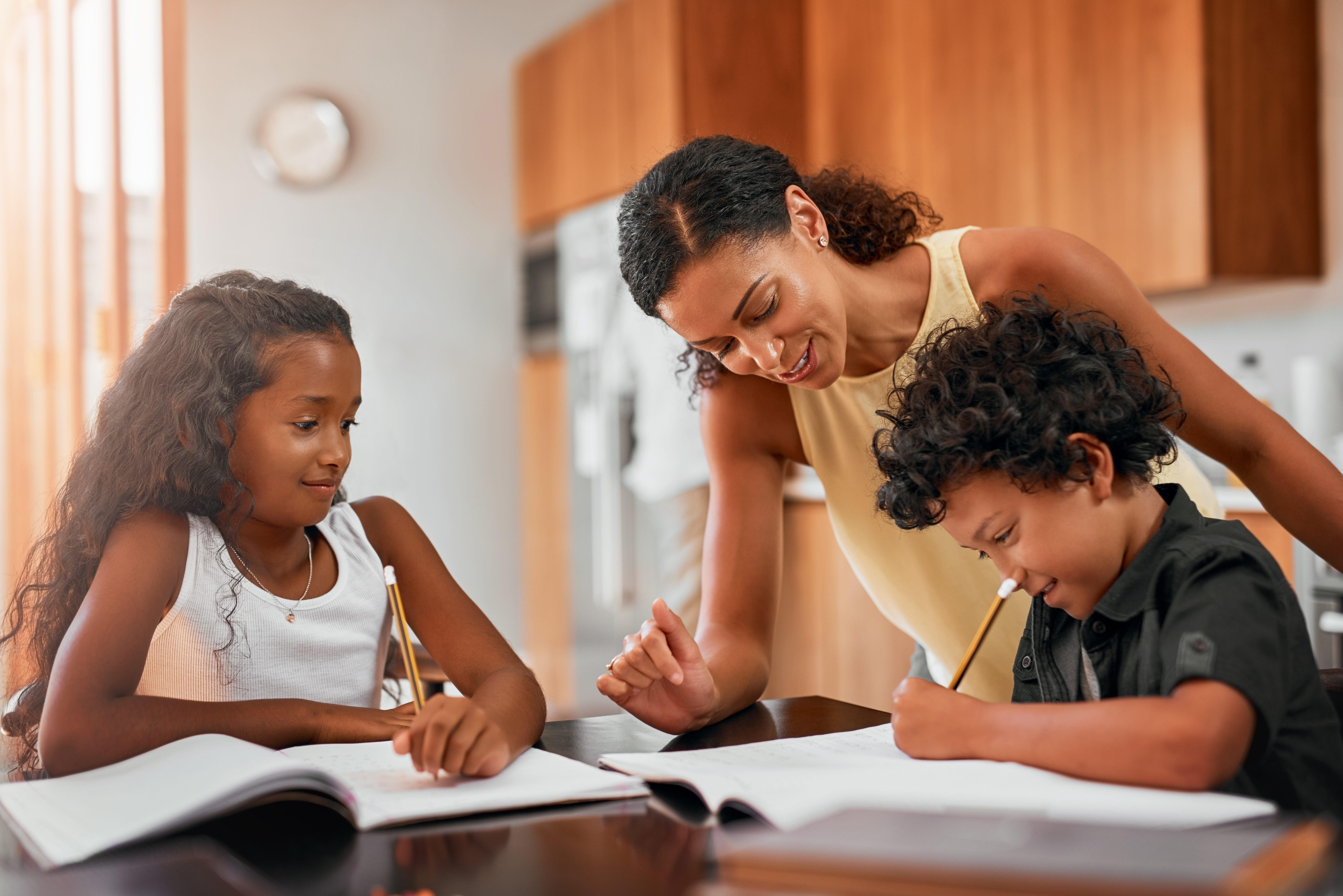 Smiling parent helping two children with their studies at the kitchen table.