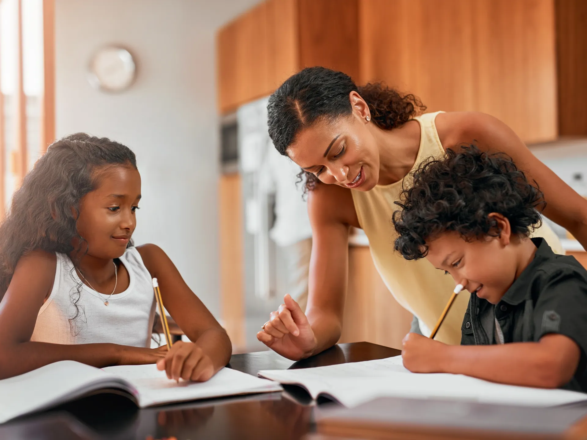 Smiling parent helping two children with their studies at the kitchen table.