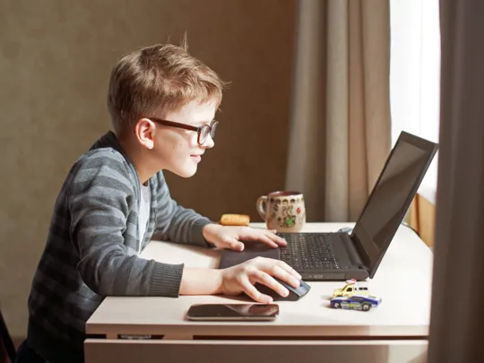 Young boy wearing glasses engaged in an interactive learning session on his laptop during homeschooling.